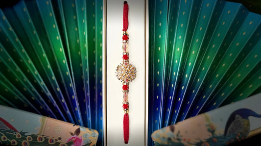 Decorative hand fan with peacock design and a red rakhi on a black background